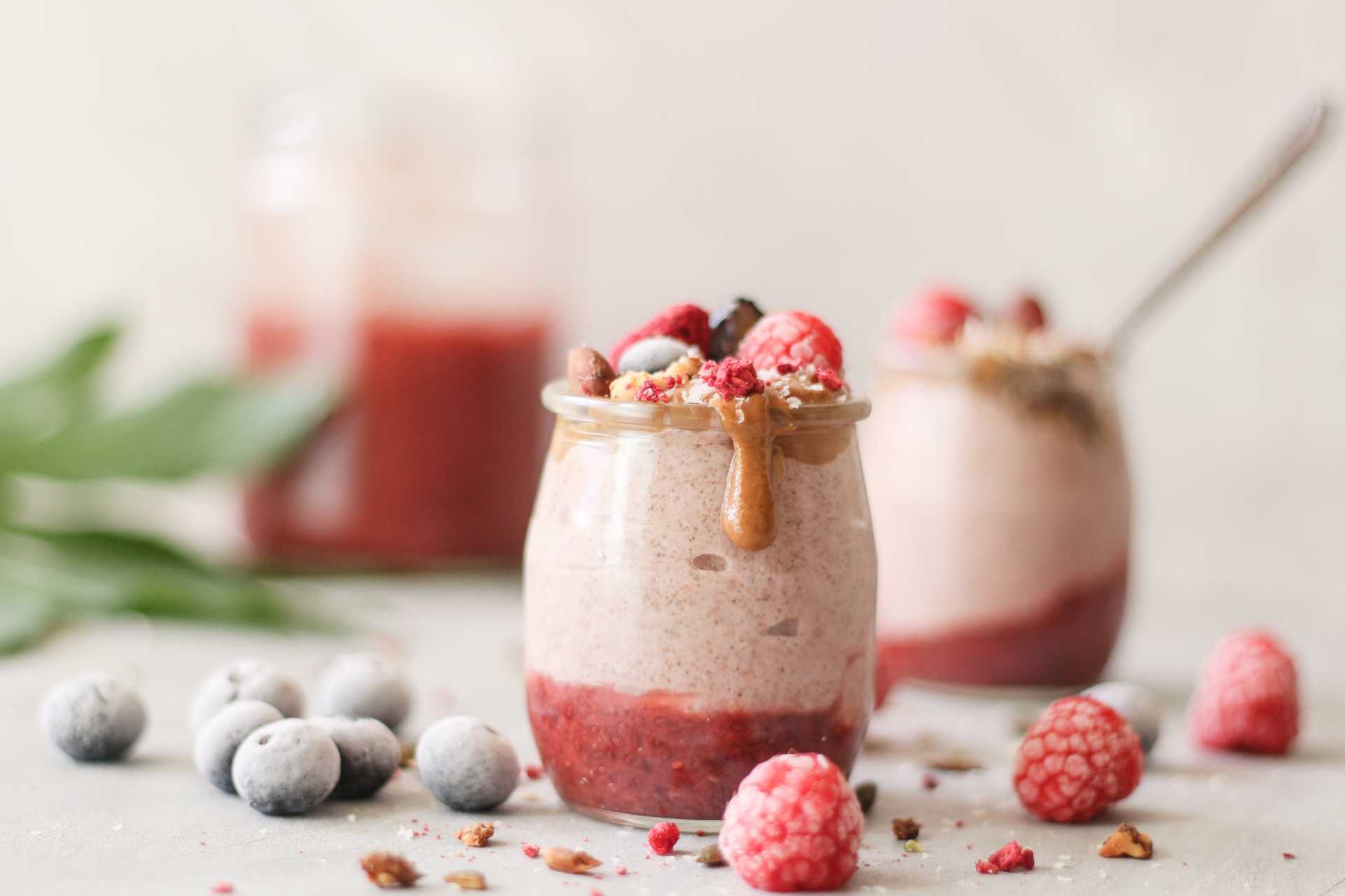 Kaksi vaaleanpunaista smoothielasia, joiden edessä jäisiä mustikoita ja vadelmia